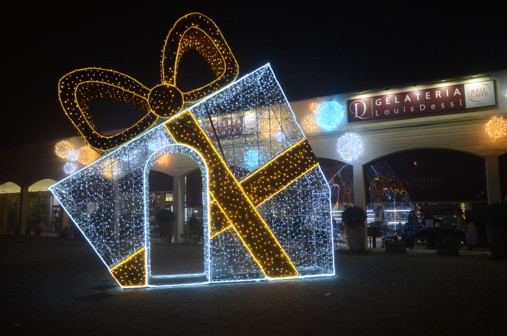 Grande pacco regalo luminoso davanti a una pasticceria